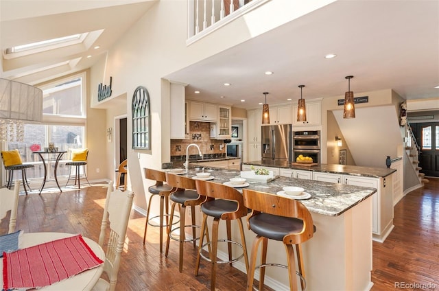 kitchen with appliances with stainless steel finishes, pendant lighting, tasteful backsplash, dark stone counters, and dark wood-type flooring