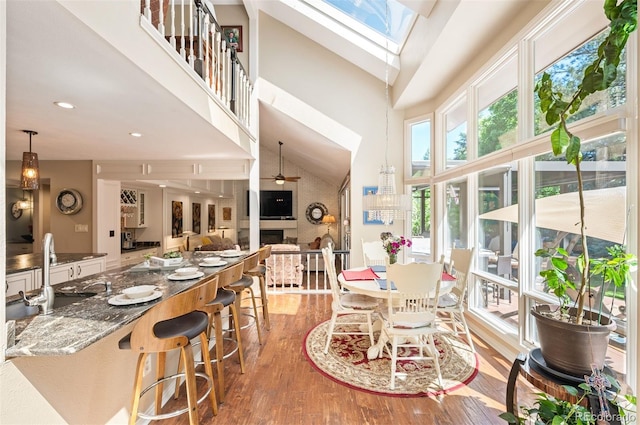 dining area featuring high vaulted ceiling, a skylight, sink, ceiling fan, and light hardwood / wood-style floors