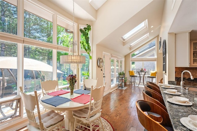 dining space with sink, a skylight, high vaulted ceiling, and wood-type flooring