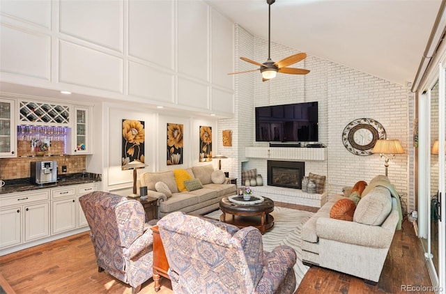 living room with high vaulted ceiling, a fireplace, ceiling fan, dark wood-type flooring, and bar area