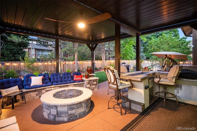 view of patio featuring area for grilling, a fire pit, ceiling fan, and exterior bar