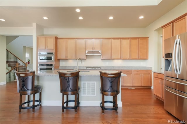 kitchen featuring light stone counters, light brown cabinetry, stainless steel appliances, and a kitchen bar