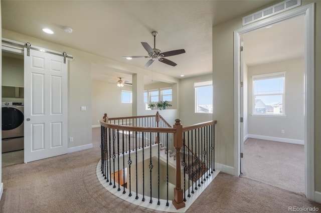 corridor featuring washer / clothes dryer, a barn door, and light carpet