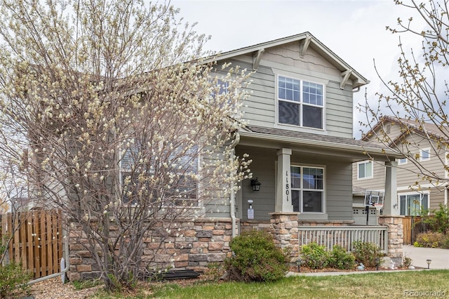 craftsman inspired home featuring covered porch, fence, and stone siding