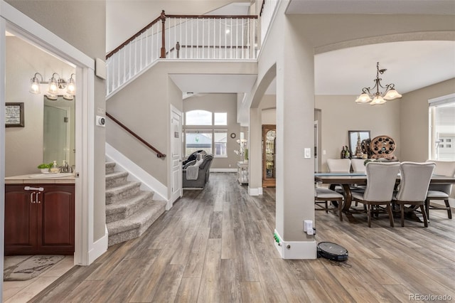 entrance foyer with stairs, wood finished floors, a high ceiling, arched walkways, and a notable chandelier