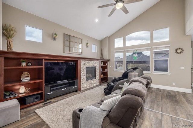 living room with a ceiling fan, a tiled fireplace, wood finished floors, high vaulted ceiling, and baseboards