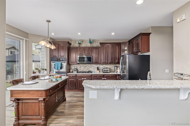 kitchen with a peninsula, light wood-style flooring, appliances with stainless steel finishes, and a kitchen bar