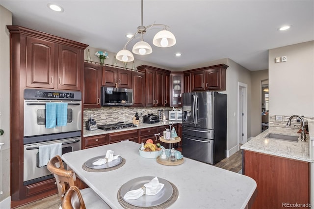 kitchen with decorative light fixtures, appliances with stainless steel finishes, tasteful backsplash, light wood-type flooring, and a sink
