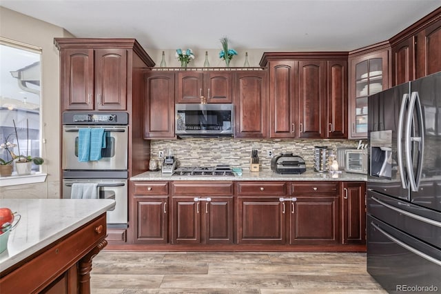 kitchen with backsplash, appliances with stainless steel finishes, light stone countertops, a toaster, and glass insert cabinets