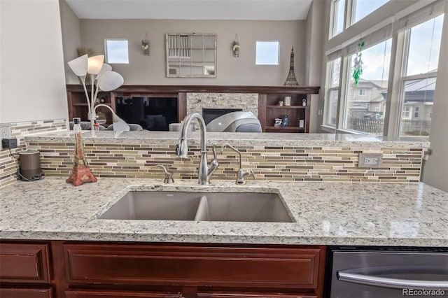 kitchen featuring tasteful backsplash, stainless steel dishwasher, a sink, light stone counters, and open floor plan