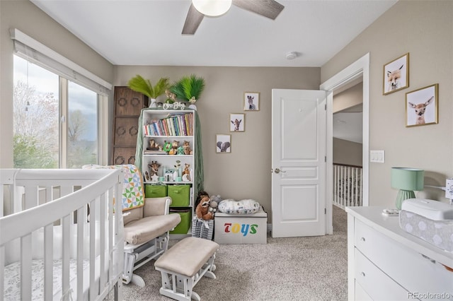 bedroom featuring light colored carpet, a ceiling fan, and a nursery area