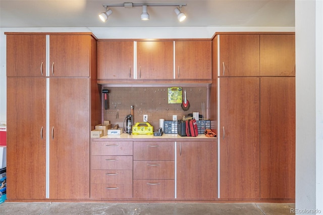 kitchen with light countertops, concrete flooring, brown cabinets, and backsplash