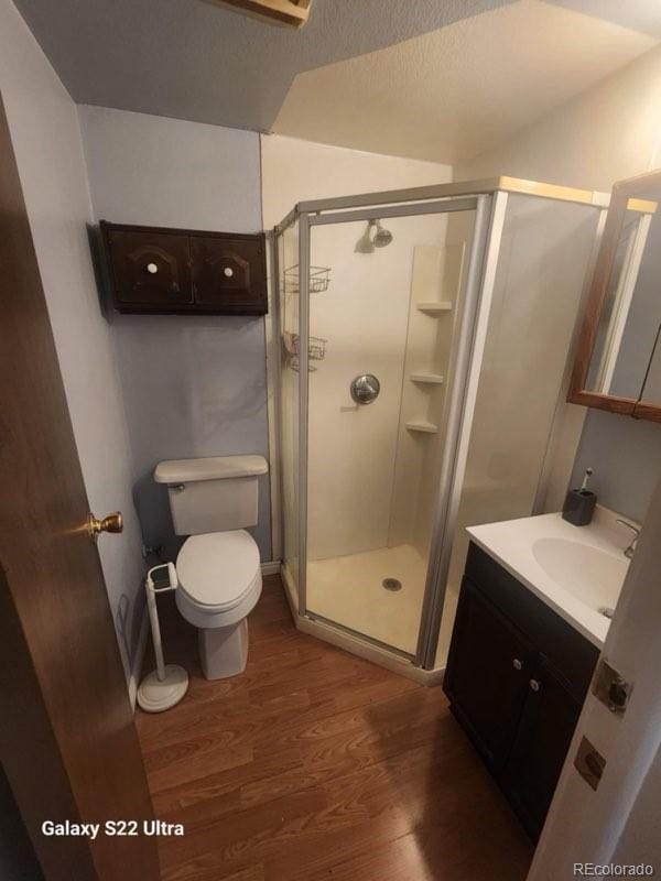 bathroom featuring hardwood / wood-style floors, a shower with door, a textured ceiling, toilet, and vanity