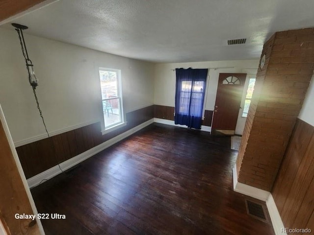 spare room featuring a textured ceiling, dark hardwood / wood-style floors, and wood walls