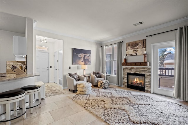 tiled living room with ornamental molding and a stone fireplace