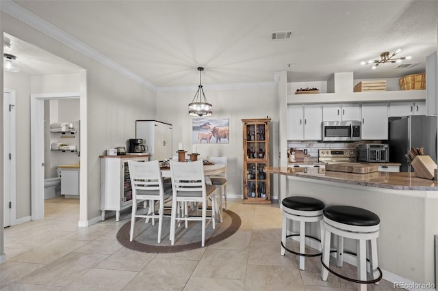 kitchen with crown molding, decorative light fixtures, dark stone counters, stainless steel appliances, and white cabinets