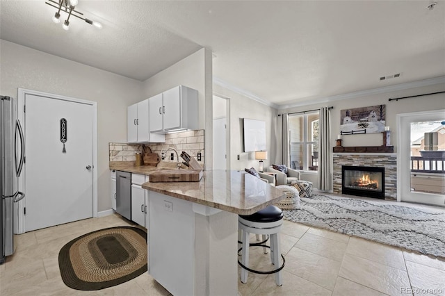 kitchen with appliances with stainless steel finishes, white cabinetry, a breakfast bar area, decorative backsplash, and kitchen peninsula