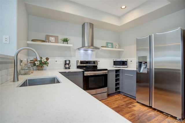 kitchen with sink, stainless steel appliances, wall chimney range hood, tasteful backsplash, and a tray ceiling