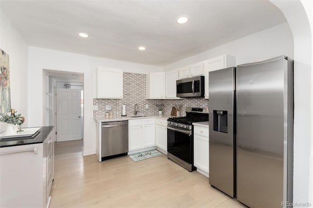 kitchen featuring tasteful backsplash, white cabinets, appliances with stainless steel finishes, light wood-style floors, and a sink