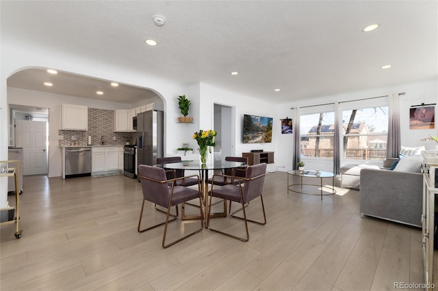 dining space with arched walkways, light wood finished floors, a textured ceiling, and recessed lighting