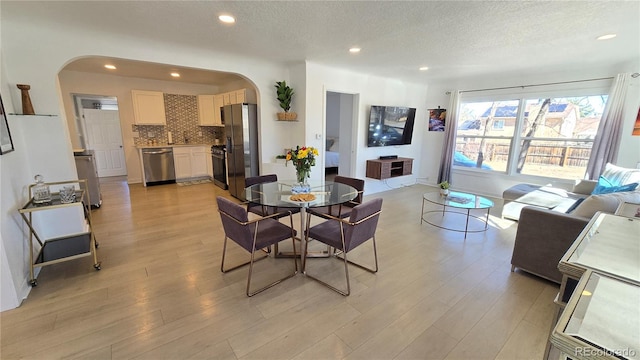 dining room with arched walkways, light wood-style flooring, a textured ceiling, and recessed lighting