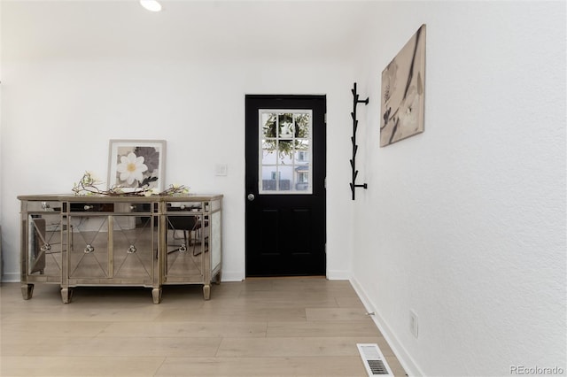 foyer with light wood-type flooring, visible vents, and baseboards