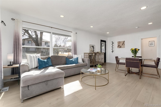 living area with a textured ceiling, visible vents, light wood-style flooring, and recessed lighting