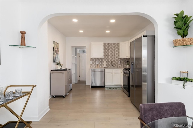 kitchen featuring arched walkways, stainless steel appliances, white cabinetry, light wood finished floors, and tasteful backsplash