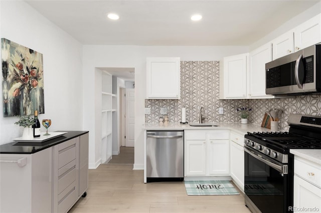 kitchen with a sink, light wood-style floors, white cabinets, appliances with stainless steel finishes, and backsplash