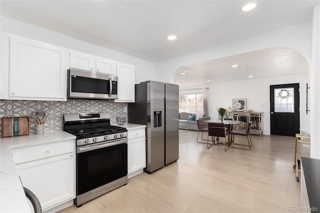 kitchen featuring arched walkways, stainless steel appliances, light countertops, backsplash, and white cabinets