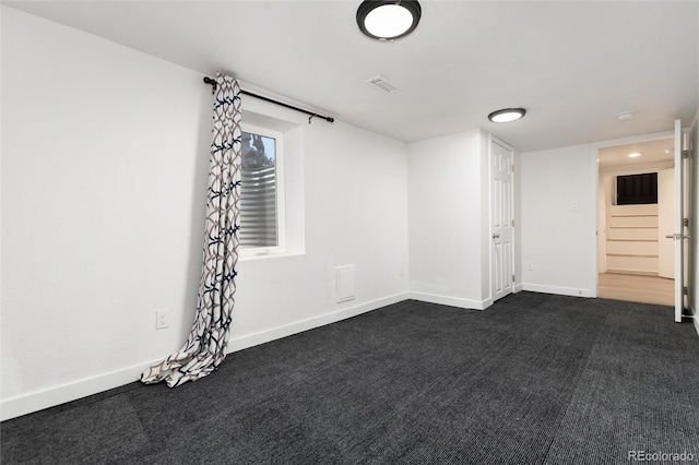 spare room with stairs, dark carpet, visible vents, and baseboards