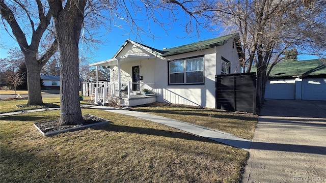 view of front facade with covered porch, a garage, driveway, stucco siding, and a front yard