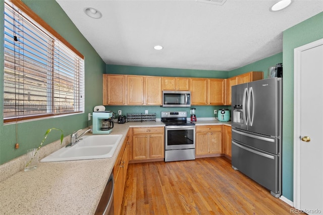 kitchen with light brown cabinetry, sink, stainless steel appliances, and light hardwood / wood-style floors