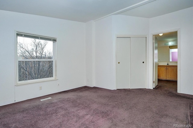 unfurnished bedroom featuring dark colored carpet, ensuite bath, and a closet