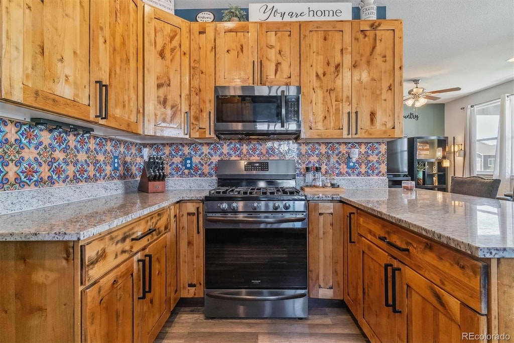 kitchen with light stone countertops, ceiling fan, dark wood-type flooring, stainless steel appliances, and tasteful backsplash