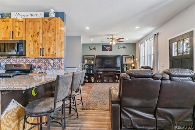 living room with ceiling fan, a textured ceiling, and light wood-type flooring