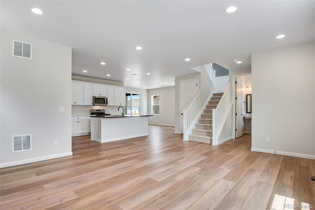 kitchen with white cabinetry, tasteful backsplash, light wood-type flooring, appliances with stainless steel finishes, and an island with sink