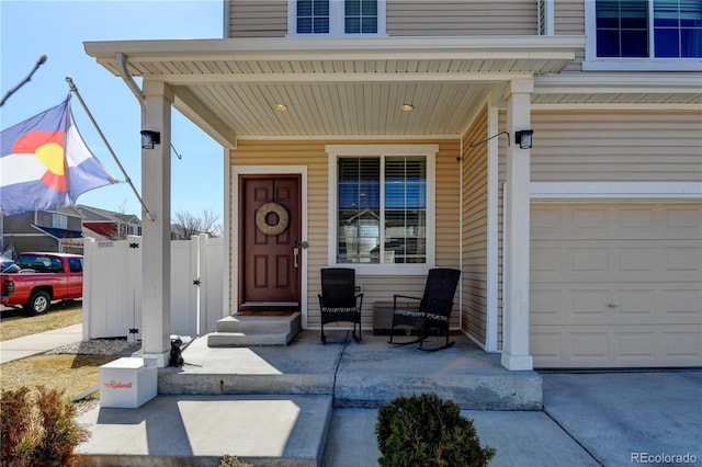 view of exterior entry featuring a garage, fence, and covered porch