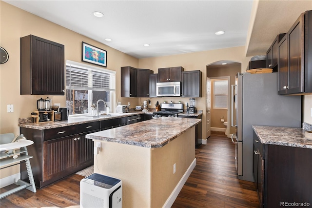 kitchen featuring arched walkways, appliances with stainless steel finishes, dark wood-type flooring, and a sink