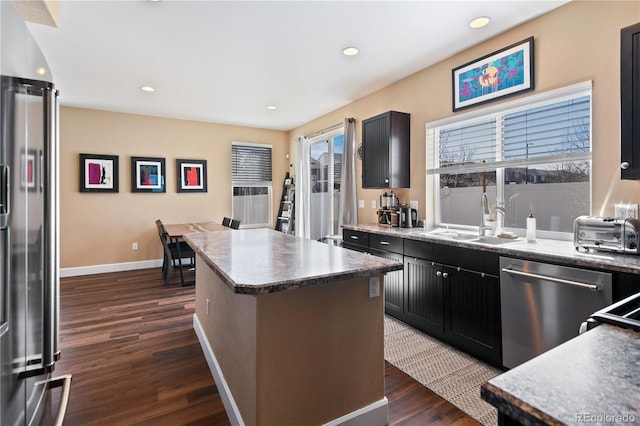 kitchen featuring a sink, a kitchen island, baseboards, appliances with stainless steel finishes, and dark wood-style flooring