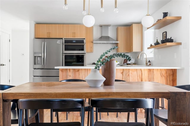 kitchen featuring wall chimney exhaust hood, double oven, stainless steel fridge, and light countertops