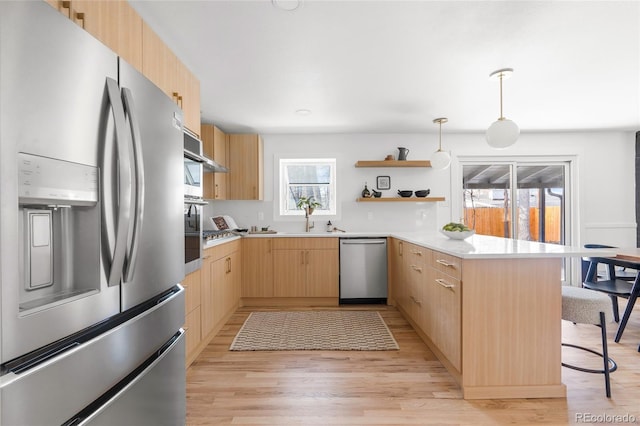 kitchen with a kitchen breakfast bar, a peninsula, stainless steel appliances, light brown cabinets, and a sink