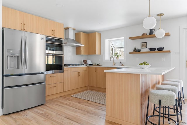 kitchen with stainless steel appliances, a peninsula, wall chimney exhaust hood, and light brown cabinetry