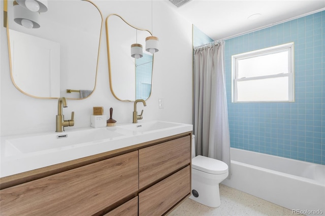 bathroom featuring toilet, double vanity, a sink, and speckled floor