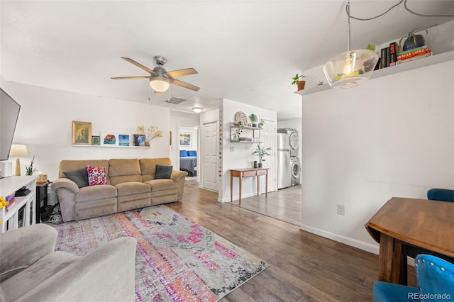 living room with dark hardwood / wood-style flooring, stacked washing maching and dryer, and ceiling fan