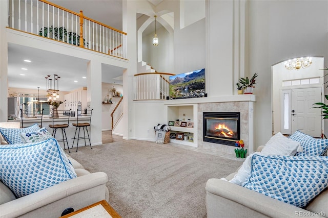 carpeted living room with baseboards, stairway, an inviting chandelier, a high ceiling, and a fireplace