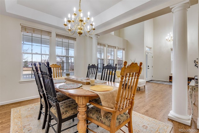 dining room with light wood finished floors, a raised ceiling, a wealth of natural light, and ornate columns