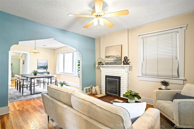 living room with a textured ceiling, wood-type flooring, ceiling fan, and a brick fireplace