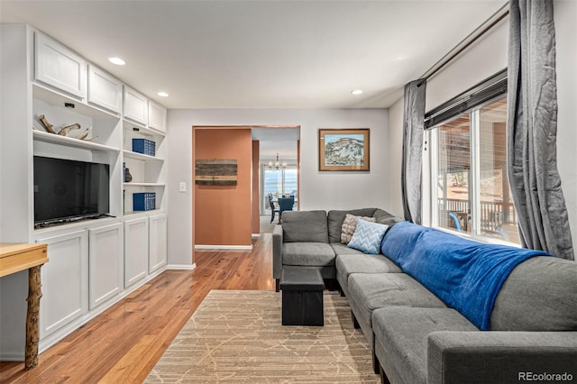 living room with built in features, light hardwood / wood-style floors, and an inviting chandelier