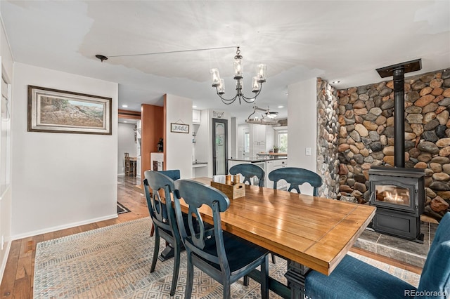 dining space with wood-type flooring, a wood stove, and a notable chandelier